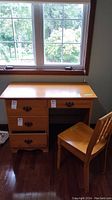 Desk with three drawers, natural wood finish, sitting by window on wood floor