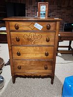Front view of wood dresser showing four drawers with carved details and wooden knobs, surface scratches visible.