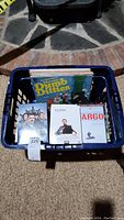 Blue basket containing DVDs including The Dumb Ditties, Blue Bloods Season 3, The Office Season 3, and Fargo
