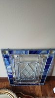 Full view of leaded glass panel angled, showing blue and clear textured glass design, placed on wooden floor against wall.