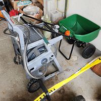 Suncoast hose caddy holding black garden hose and Scotts fertilizer spreader with green hopper side angle