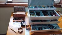 Open light blue metal jewelry box with top tray and two drawers filled with assorted jewelry, wooden box, clutch purse and bracelets on shelf