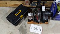 Photo of Jobmate mitre saw and black plastic toolbox on concrete floor with instruction manual.