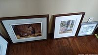 Group photo of three framed prints leaning against wall showing their relative sizes and framing.