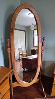 Front view of full length oval mirror with pine frame showing mirror surface and stand.