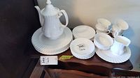Full set of Royal Albert white china including teapot, plates, cups, creamer, and sugar bowl arranged on a dark surface.