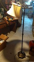 Full view of vintage floor lamp showing beige fabric shade and tall metal stand in a basement setting.