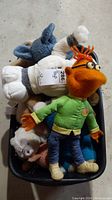 Plastic bin with multiple stuffed toys including Scooter doll from The Muppet Show, a Gund teddy bear, and other plush figures