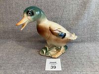 Front angled view of glazed ceramic duck figurine on fabric backdrop with lot card