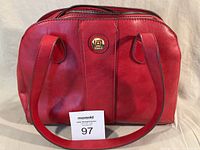 Front view of red faux leather handbag showing logo hardware and handles