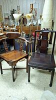 Set of two Asian corner style chairs made of mahogany and rosewood, with lamps and other furniture in background.