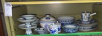 Shelf with multiple blue and white porcelain items including pedestal bowls, tureen, bowls, lidded jars, plates, pitcher, ladle