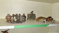 Top shelf view showing multiple figurines and carved pieces arranged horizontally on a white shelf.