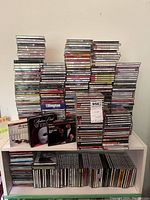 Photo showing multiple stacks of music CDs on top of a white shelving unit. Several rows of CDs are visible with spines showing various artist and album names.