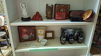 Overview of shelf showing porcelain, ceramic and wooden Buddha figurines alongside lacquerware box