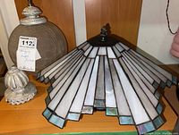 Photo showing the stained glass light fixture with geometric white and blue glass panels next to the globe light fixture on a wooden surface.