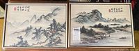 Two framed Asian silk paintings side by side depicting mountain and riverside scenes with calligraphy and red stamps