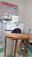 Singer Magic Press MP4 ironing press with original box on top of a washing machine; wooden drying rack leaning against the machine.