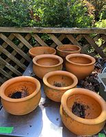 Six terra cotta pots displayed on a metal surface outdoors, showing weathering and soil residue inside each pot.