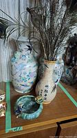 Three porcelain vases, small ceramic dish and peacock feathers grouped together