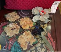 Four square pressed flower coasters and a large flower sculpture displayed on table.