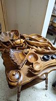 Table displaying multiple Monkey Pod wood bowls, serving pieces, and utensils stacked and arranged