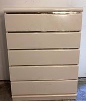 Front view of 5 drawer cream laminate dresser showing gold accent trim and some surface marks.
