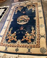 Full view of the rectangular area rug showing cream border, blue field with five dragons, decorative border patterns, and fringe on edges.