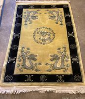 Full view of the plush rug showing yellow interior with black border and five gray dragons, along with fringes on ends.