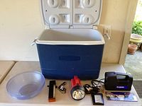 Overview of cooler with accessories in front including bowls, flashlight, air pump and small tools