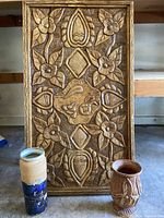 Full view of the carved wooden wall art panel flanked by the two vases placed on the floor.