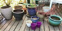 Overview of all 11 planter pots arranged on deck showing various sizes, colors, and materials, including ceramic and terracotta pots