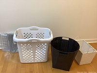 White plastic laundry basket, black woven basket, and white woven basket grouped on floor next to stacked closet dividers.