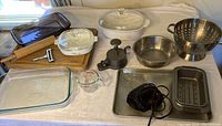 Overview of all kitchen items spread out on a white tablecloth including mixer, bakeware, and utensils.