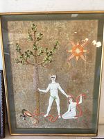Photo of framed mixed media Adam and Eve artwork showing details of figures, tree with beads, serpent, and star on gold background