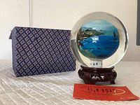 Glass ball showing the painted Oregon coast seascape inside, placed on the carved wooden stand with fabric-covered box behind.
