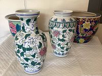 Four ceramic items including two tall vases with green ivy and pink flowers, a large colorful planter with butterflies and birds, and a smaller green planter with pink flowers.