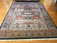 Full view of rug on hardwood floor showing overall dimensions, border and fringe
