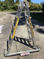 View of the Little Giant ladder standing on concrete, showing dual-sided rungs and yellow locking mechanisms, with Wingspan stabilizer attached to base.