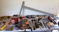 Wide view of the table showing the assortment of hand tools including screwdrivers, saws, squares, level, clamps, hole saw set, and other small hand tools mostly laid out in an organized manner.