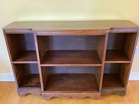 Front view of wooden shelf showing open compartments, decorative bottom edge, and front swoop.