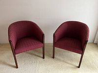 Pair of tub chairs with curved backs upholstered in red patterned fabric; wooden legs visible.