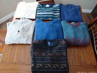 Seven men's sweaters laid out on a table showing various colors and patterns, demonstrating variety and condition.