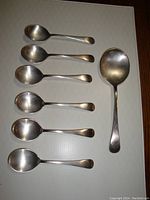 Top view of all spoons laid out on a flat surface showing 6 soup spoons and 1 serving spoon