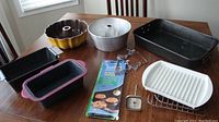 Full bakeware set including pans, racks, meat thermometer, and bakeware liner displayed on table.