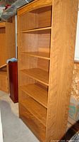 Front and right side view of the wooden bookshelf showing six shelves and some wear on the shelves and back panel holes.
