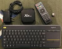 Photo of Logitech K400+ wireless keyboard, X96 Mini TV box, remote control, power adapter, and USB dongle all laid out on a surface.