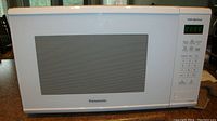 Front view of white Panasonic microwave with vented glass door and control panel showing timer LCD and buttons.