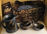Collection of Pinecroft Pottery items displayed together showing small pouring jug, two small bowls, serving utensil, and a large salad bowl with distinctive dark glaze.