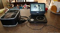 Full view of RCA portable DVD player with swivel screen on plus JVC headphones and carrying case on kitchen counter